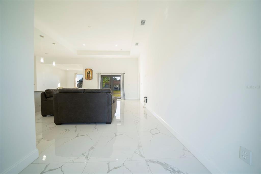 A bright living room features white marble-look tile flooring and a dark gray sofa — 2915 5TH STREET SW, LEHIGH ACRES, FL
