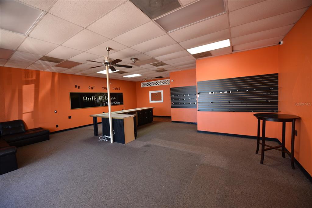 An empty retail space features orange walls, a drop ceiling, and a central service counter — 5126 US HIGHWAY 19, NEW PORT RICHEY, FL