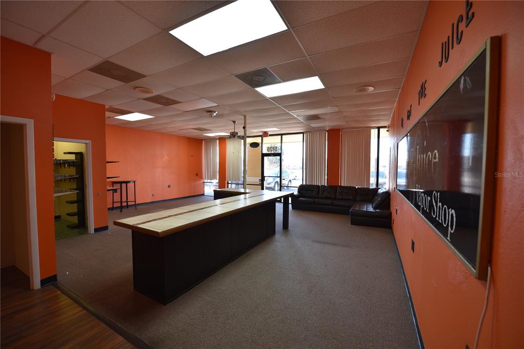 An empty commercial space features orange walls, a central counter, and a dark leather sofa — 5126 US HIGHWAY 19, NEW PORT RICHEY, FL