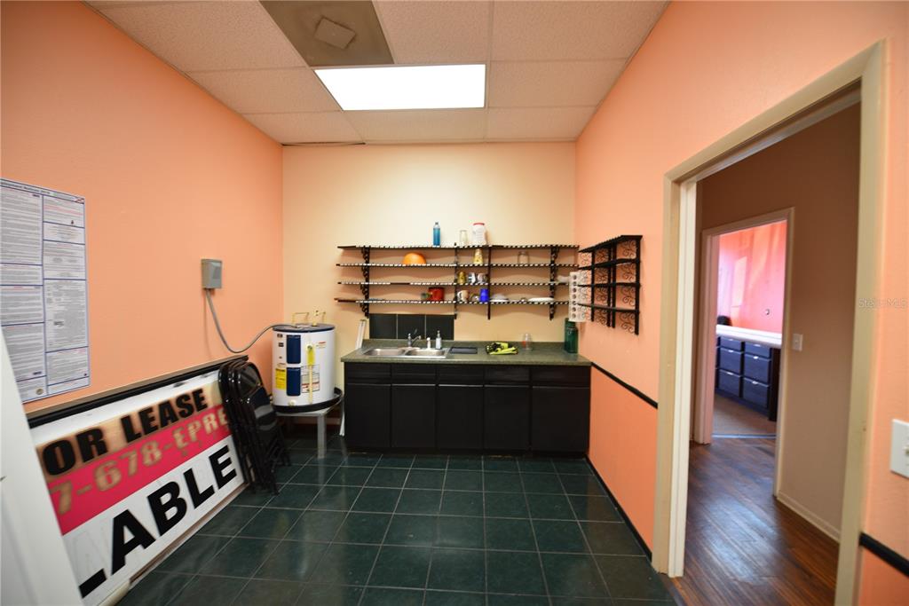 A small break room features a sink, dark cabinets, open shelving, and a water heater — 5126 US HIGHWAY 19, NEW PORT RICHEY, FL