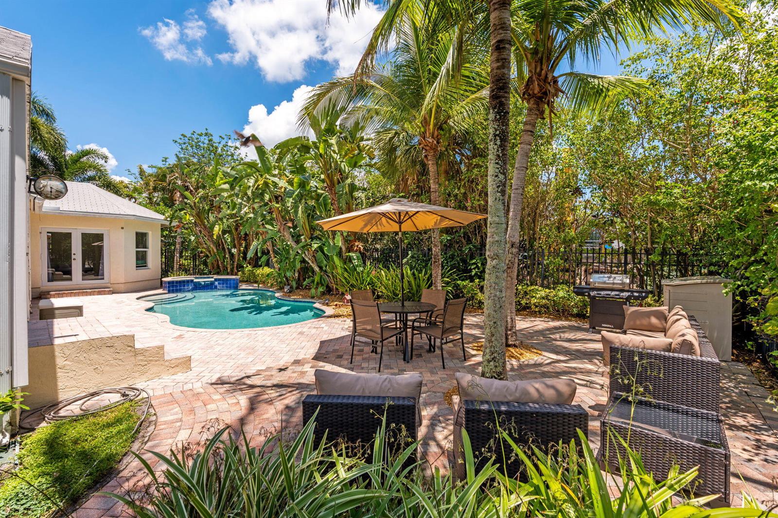 A backyard patio features a swimming pool, dining set with umbrella, and outdoor lounge furniture — 255 NE 12th Street, Delray Beach FL 33444, DELRAY BEACH, FL