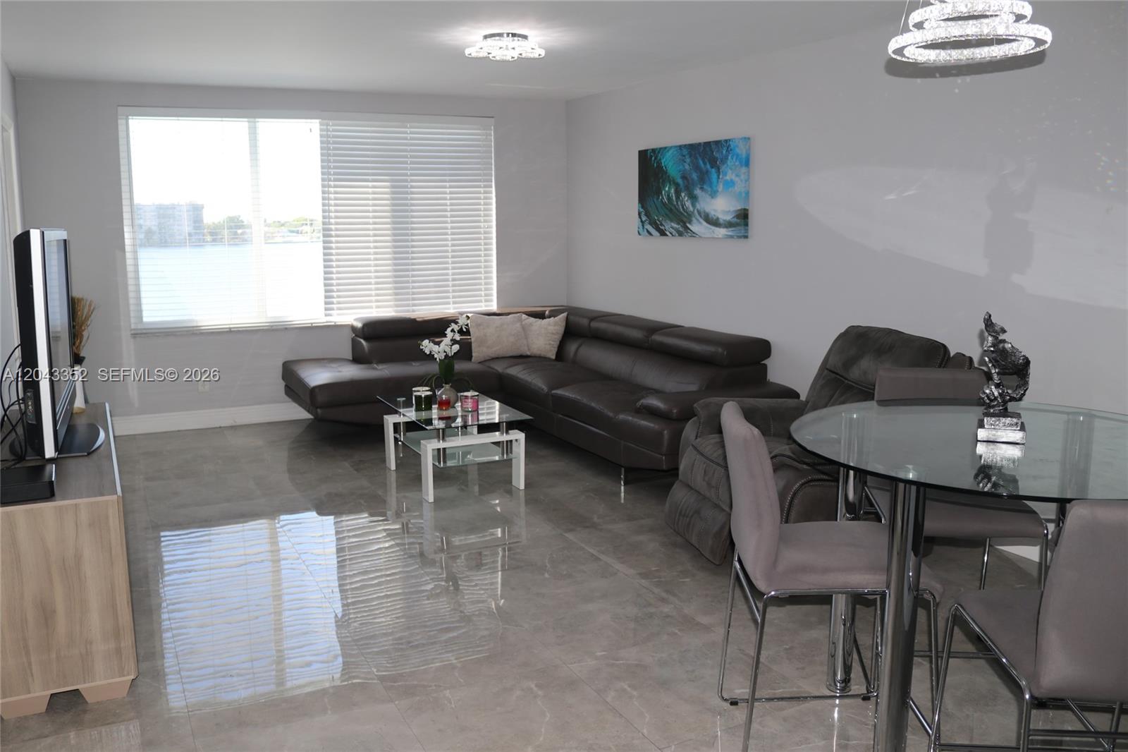 A living and dining area features gray tile floors, a dark leather sectional, and water views — 1150 NE 191st St # 37, Miami FL 33179, MIAMI, FL