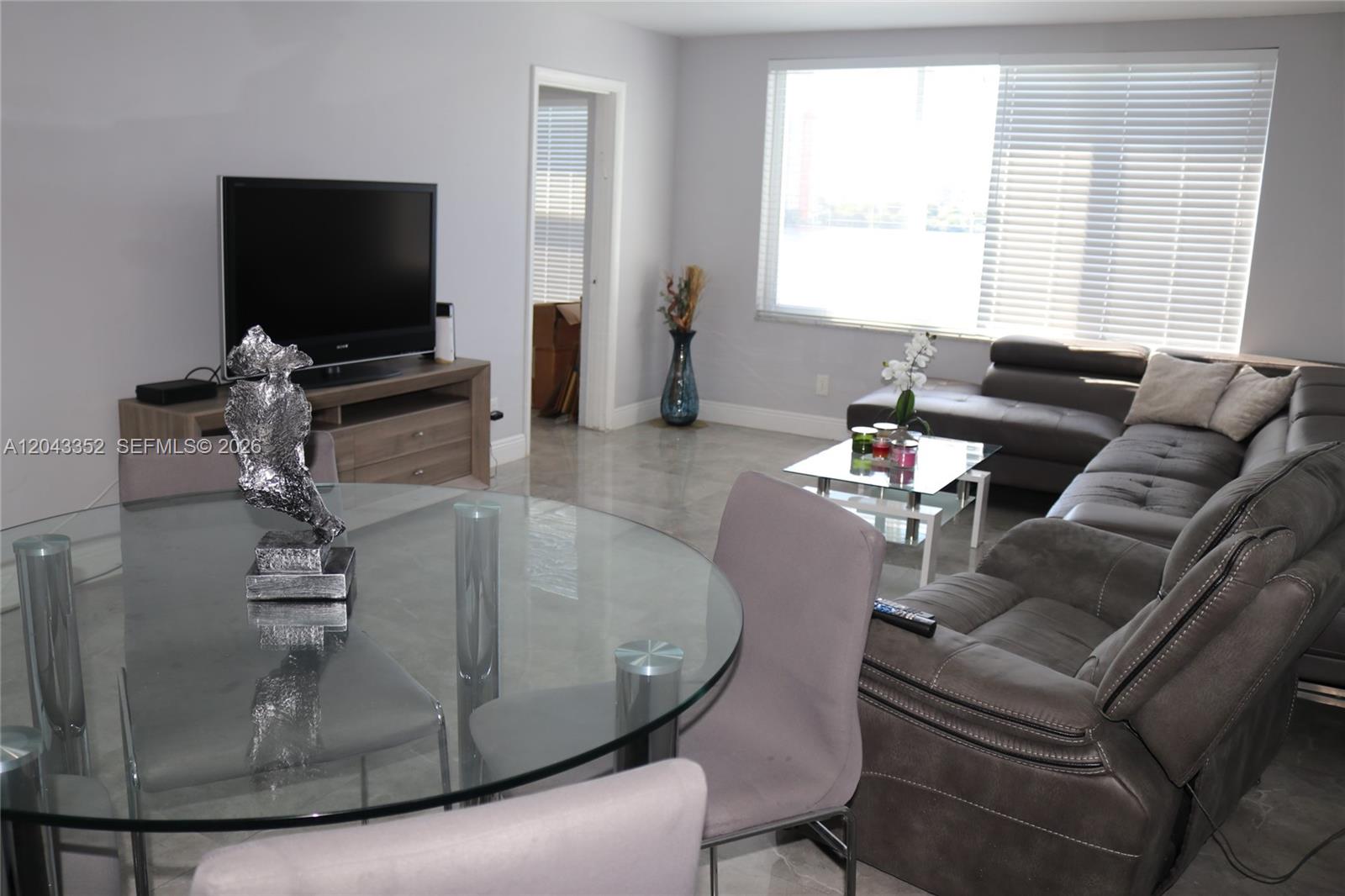 A living and dining area features a glass table, gray sofa, and large window — 1150 NE 191st St # 37, Miami FL 33179, MIAMI, FL