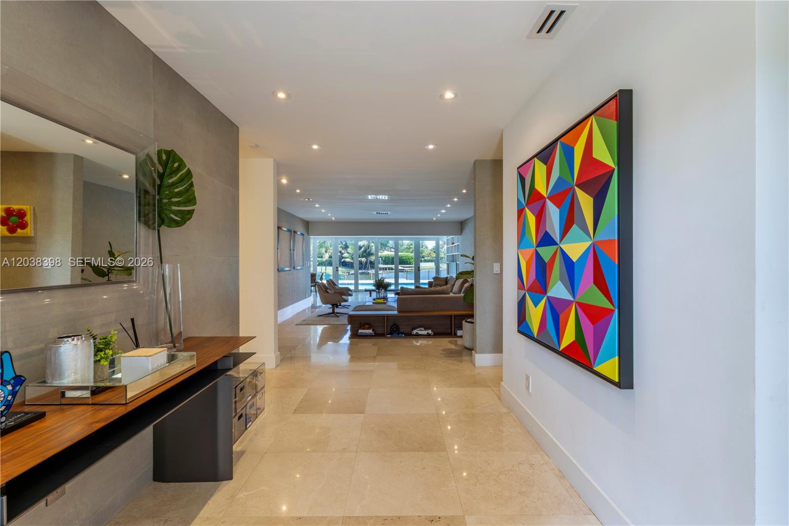 A bright hallway with marble floors leads to a living room overlooking a backyard pool — 2021 NE 212th St, Miami FL 33179, MIAMI, FL