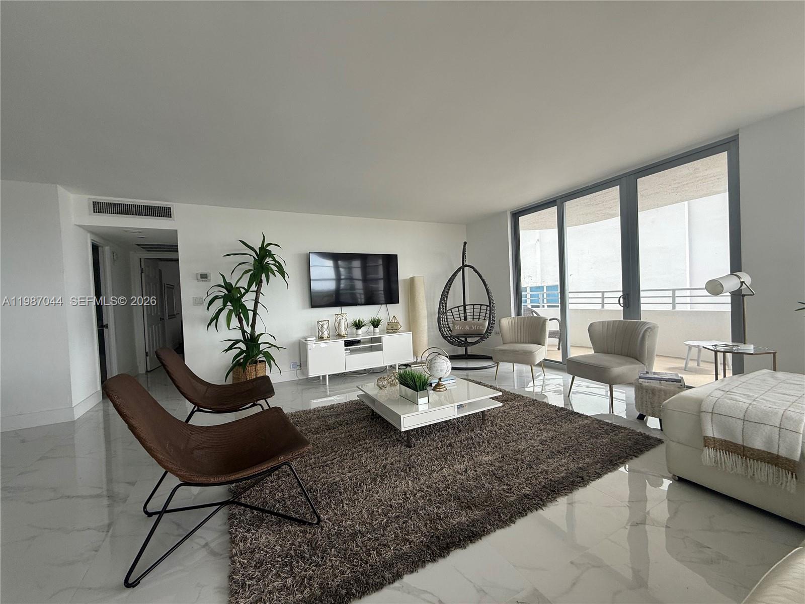 A modern living room features white marble floors, a brown area rug, and balcony access — 5555 Collins Ave # 8R, Miami Beach FL 33140, MIAMI BEACH, FL