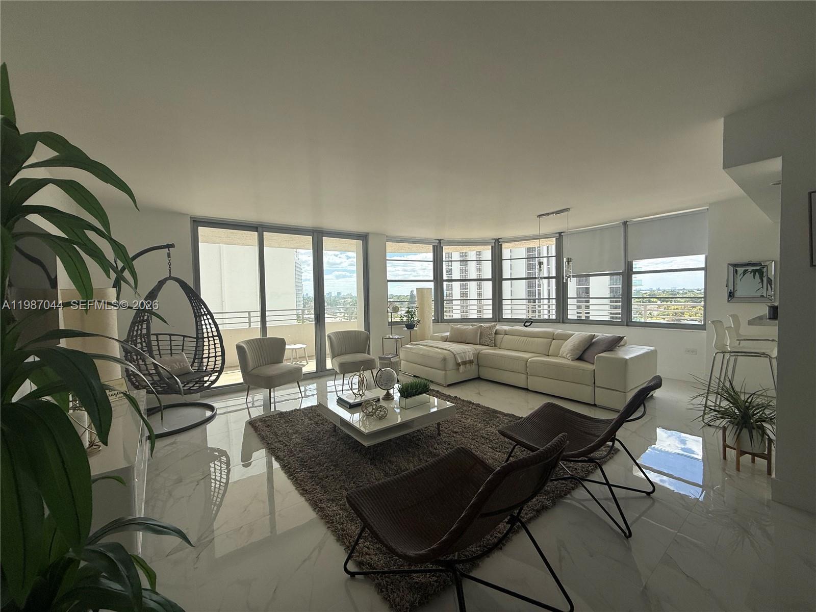 A modern living room features white marble floors, a large sectional sofa, and floor-to-ceiling windows — 5555 Collins Ave # 8R, Miami Beach FL 33140, MIAMI BEACH, FL