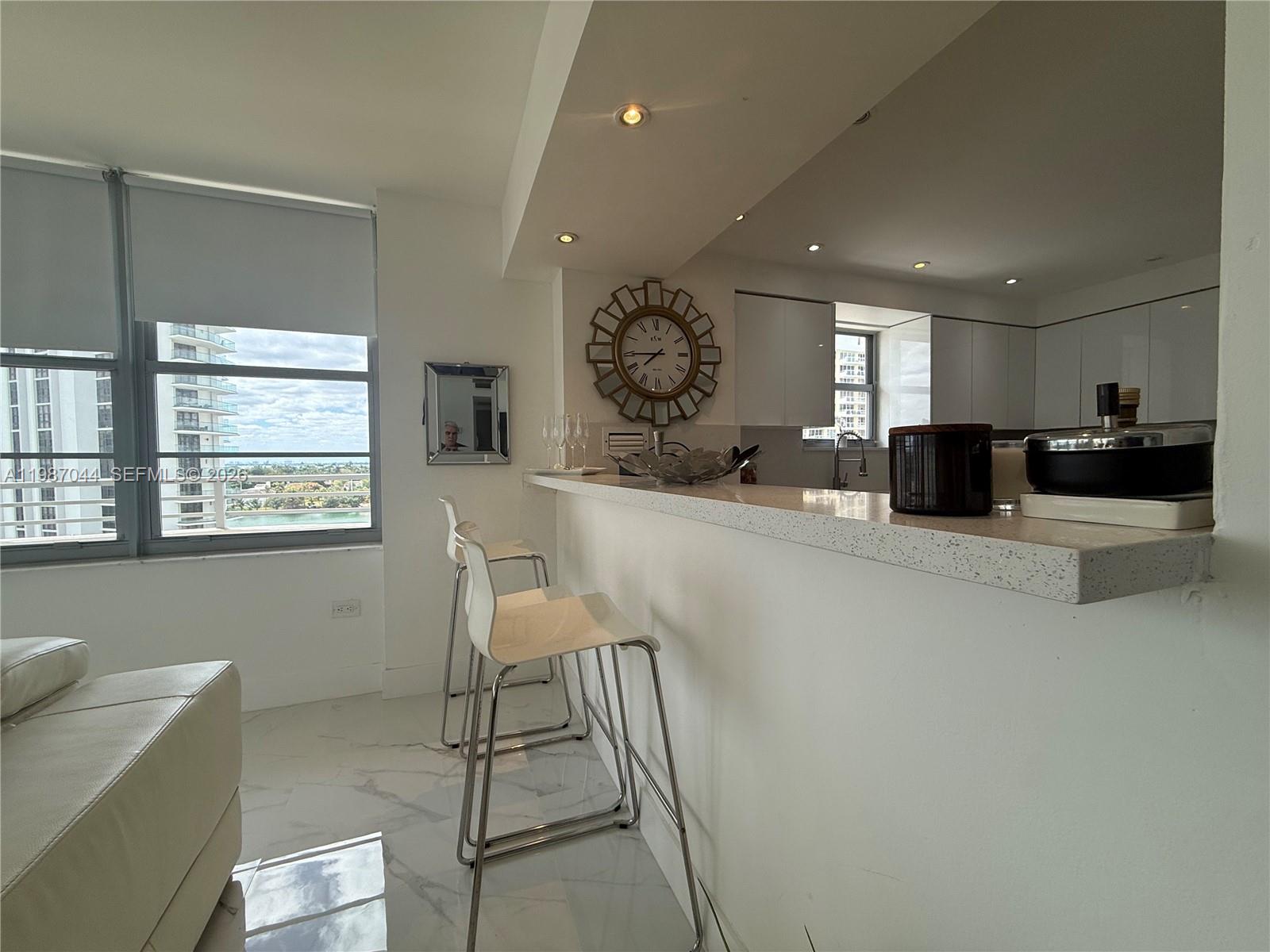 A modern kitchen features a white breakfast bar with stools and a large wall clock — 5555 Collins Ave # 8R, Miami Beach FL 33140, MIAMI BEACH, FL