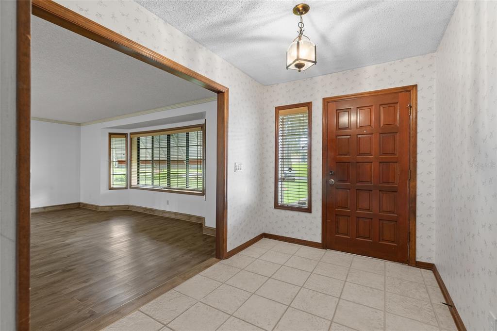 An entryway with tiled floors and wallpaper leads into a living room with wood flooring — 521 FERNWOOD DRIVE, ALTAMONTE SPRINGS, FL