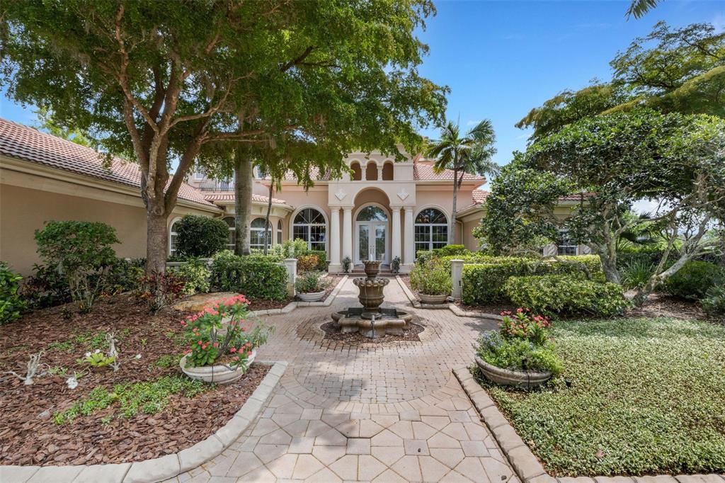 A stone walkway leads to the front entrance of a house with a central fountain — 7004 PORTMARNOCK PLACE, BRADENTON, FL