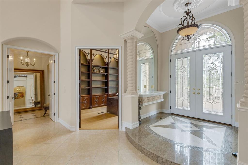 A grand foyer features a raised marble floor, double glass doors, and a built-in library — 7004 PORTMARNOCK PLACE, BRADENTON, FL