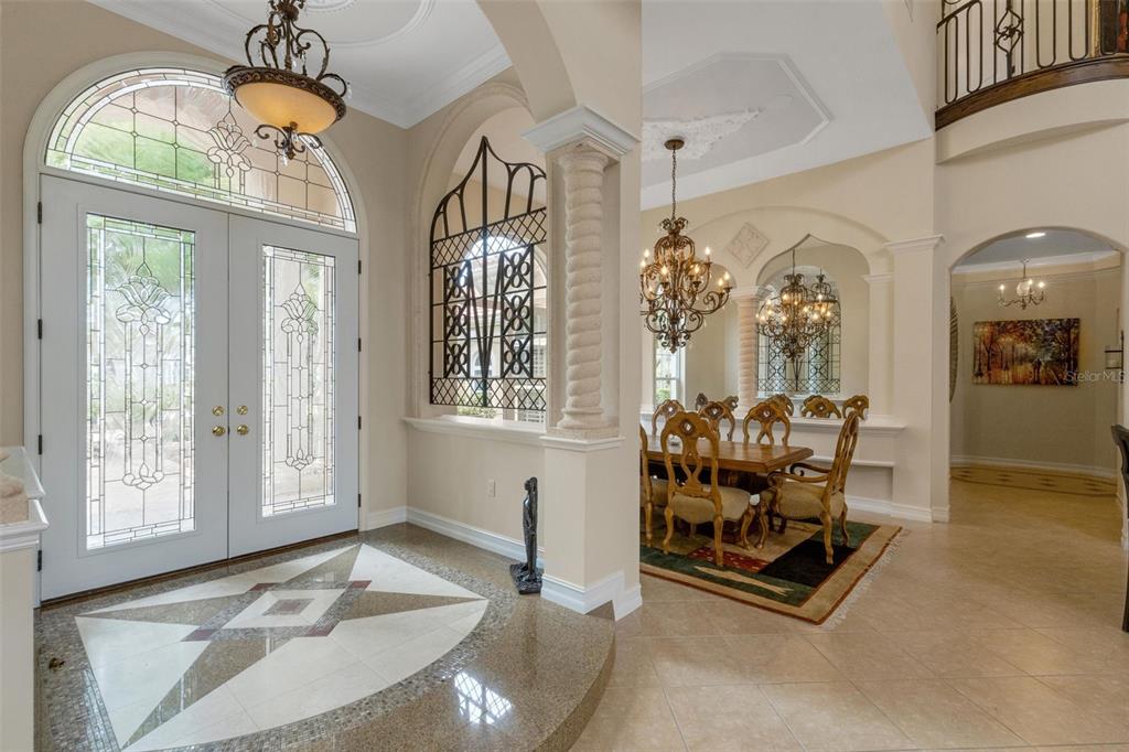 A grand foyer with a stone floor medallion leads into a formal dining room with chandeliers — 7004 PORTMARNOCK PLACE, BRADENTON, FL
