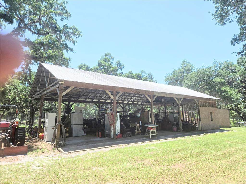 A large, open-sided metal pole barn sits on a grassy lot with a tractor nearby — 2672 SE 35TH STREET, SUMTERVILLE, FL