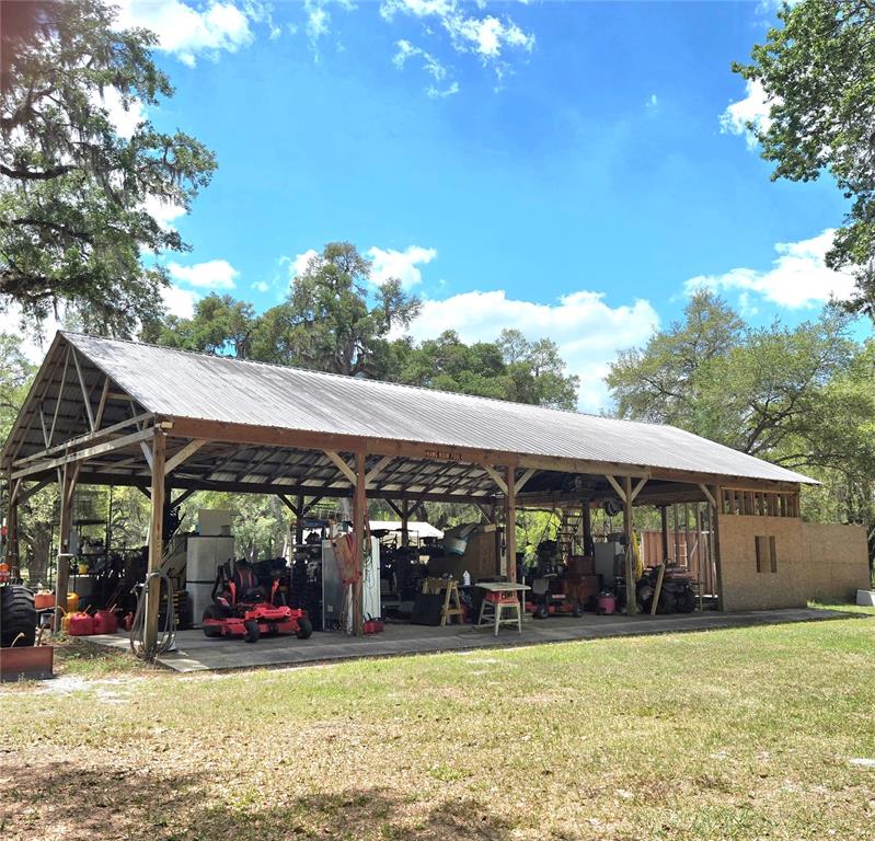 A large, open-sided metal pole barn structure sits on a grassy lot under trees — 2672 SE 35TH STREET, SUMTERVILLE, FL
