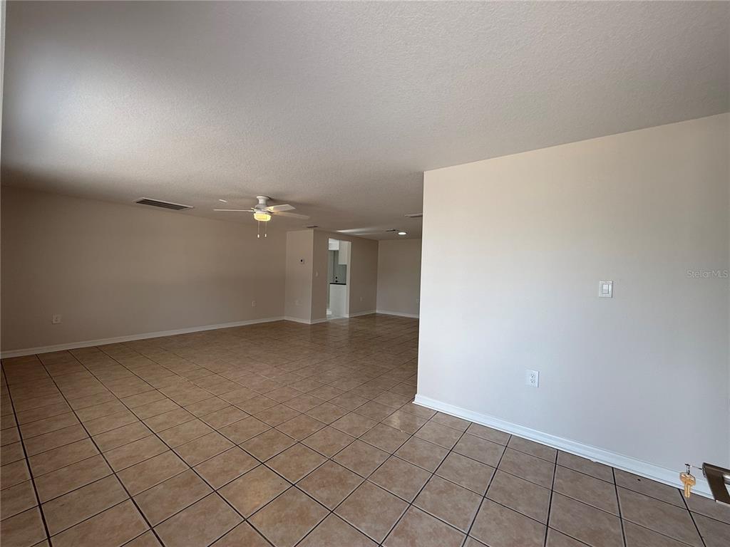 An open-concept living area features light-colored walls, a ceiling fan, and tan tile flooring — 5241 SPARROW DRIVE, HOLIDAY, FL