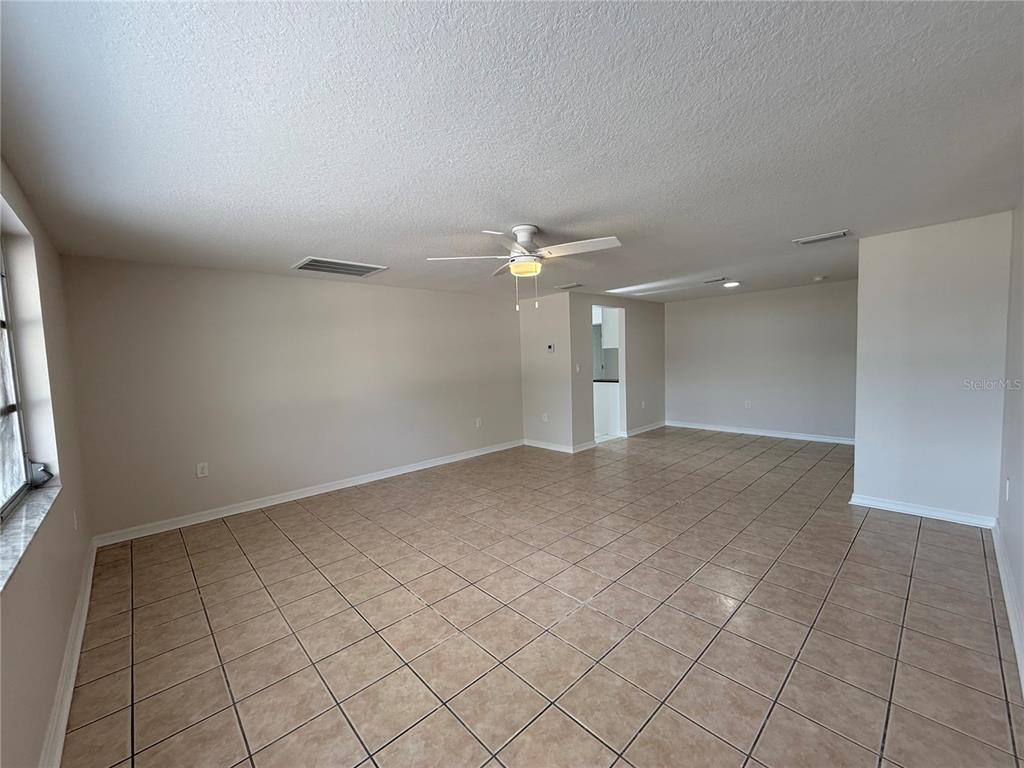 An empty living room features beige tile flooring, white walls, and a ceiling fan — 5241 SPARROW DRIVE, HOLIDAY, FL