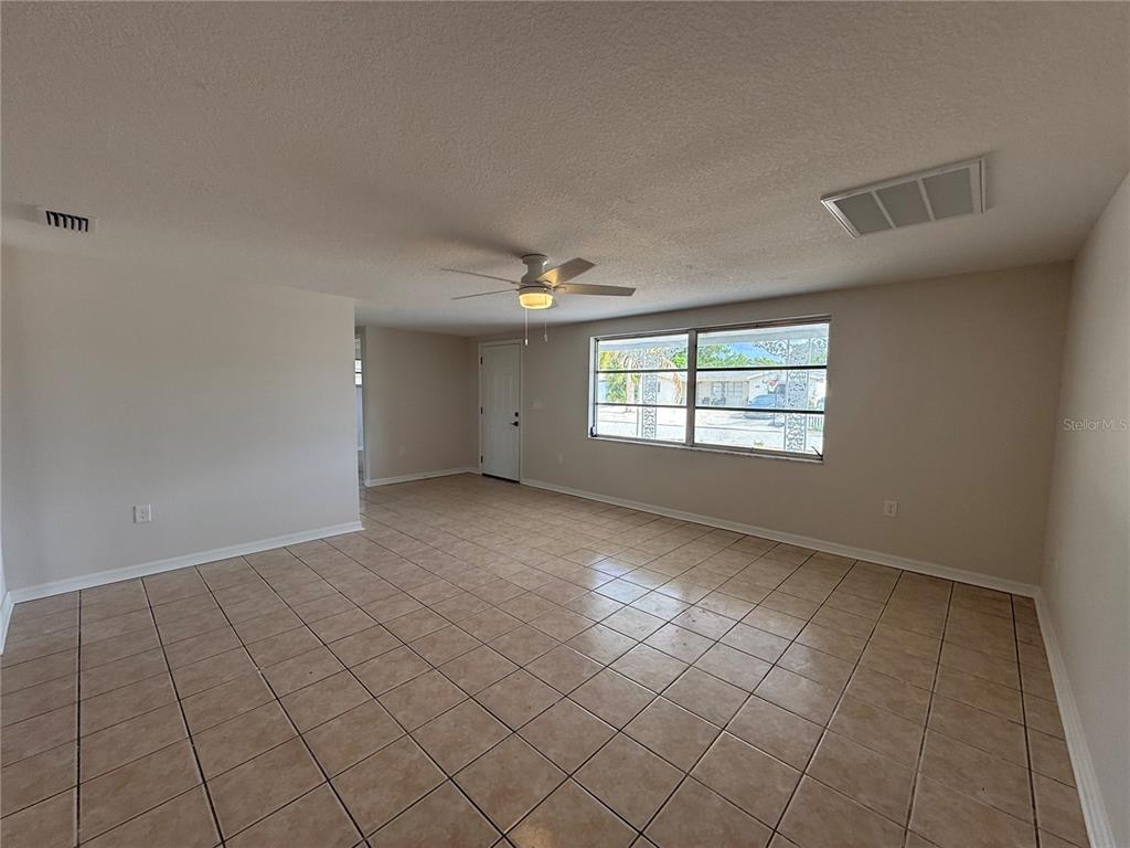 A spacious living room features light-colored tile flooring, a ceiling fan, and a large window — 5241 SPARROW DRIVE, HOLIDAY, FL