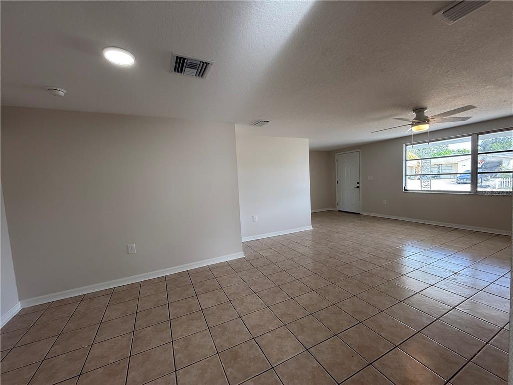 An empty room features beige walls, light-colored tile flooring, a ceiling fan, and a window — 5241 SPARROW DRIVE, HOLIDAY, FL