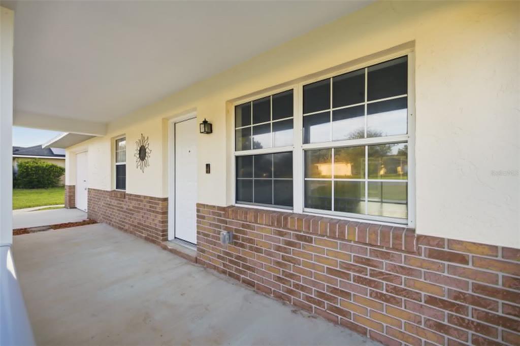 A covered porch features a brick facade, a white front door, and a large window — 3 ALMOND TRAIL PLACE, OCALA, FL