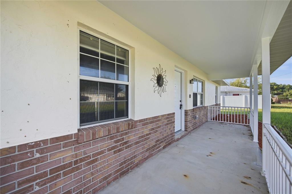 A covered porch with a brick base, white railing, and a sun wall decoration — 3 ALMOND TRAIL PLACE, OCALA, FL
