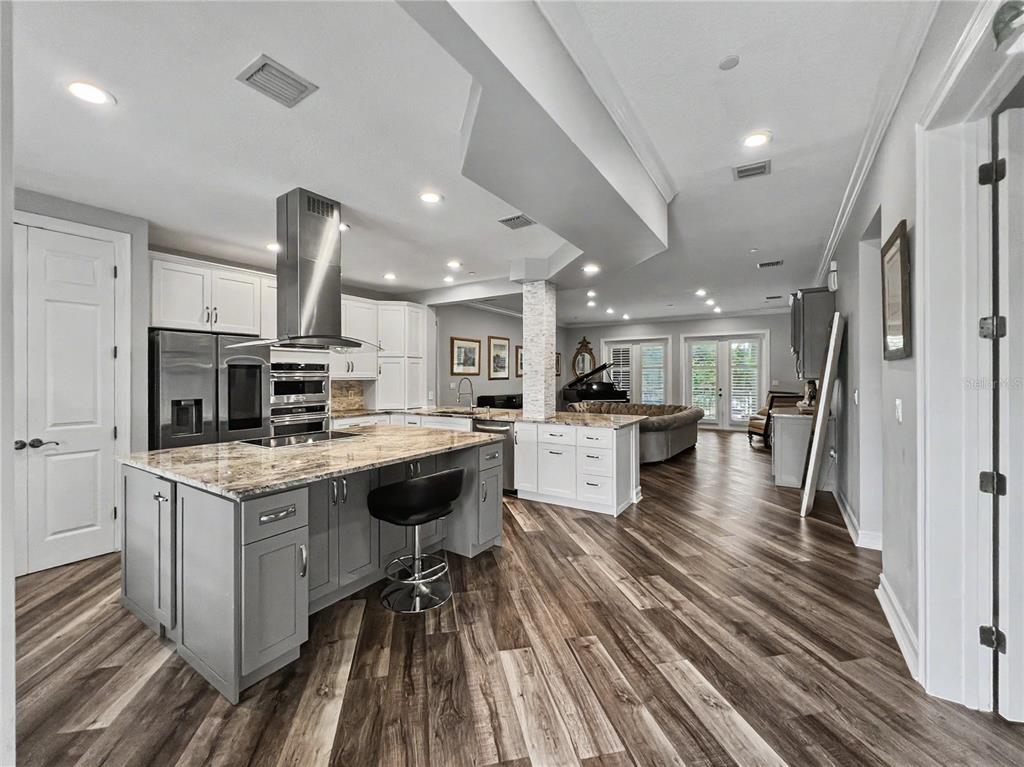 A modern kitchen with gray cabinets, a granite island, and wood-look flooring opens to a living area — 650 CAMPUS STREET UNIT 204, CELEBRATION, FL