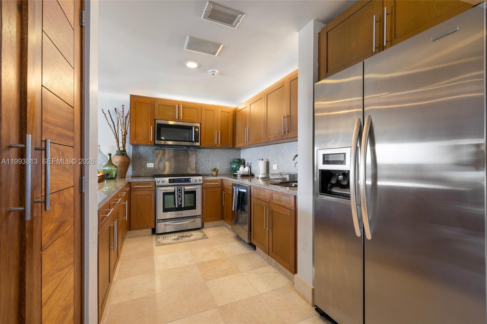 A galley kitchen features wood cabinets, stainless steel appliances, and light-colored stone tile flooring — 8101 Paseo Sotogrande # 8101, VA 23000, VA