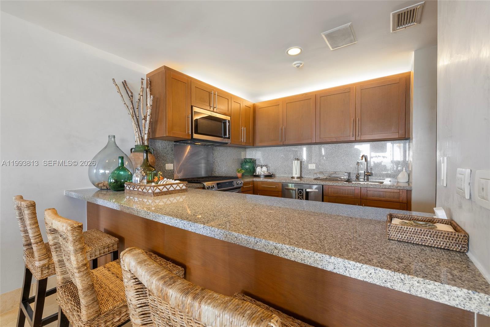 A kitchen features wooden cabinets, granite countertops, and a breakfast bar with woven chairs — 8101 Paseo Sotogrande # 8101, VA 23000, VA