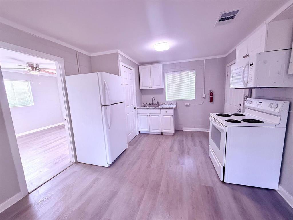 A kitchen with white cabinets, white appliances, and light-colored wood-look flooring — 2305 SW 2ND STREET UNIT A, OCALA, FL