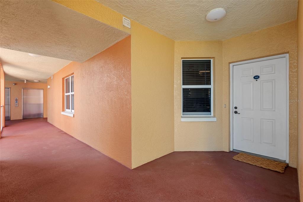 An exterior view of an apartment building hallway with a white door and yellow walls — 16550 GULF BOULEVARD UNIT 545, NORTH REDINGTON BEACH, FL