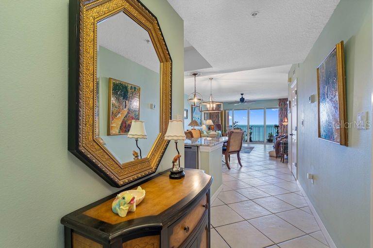 A hallway with a mirror and console table leads to an open-concept living area with ocean views — 16550 GULF BOULEVARD UNIT 545, NORTH REDINGTON BEACH, FL