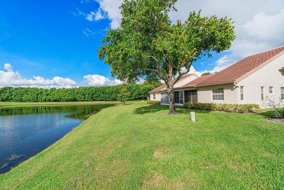 A house with a tiled roof sits beside a lake and a large tree — 7922 Sandy Pointe Drive, Delray Beach FL 33446, DELRAY BEACH, FL