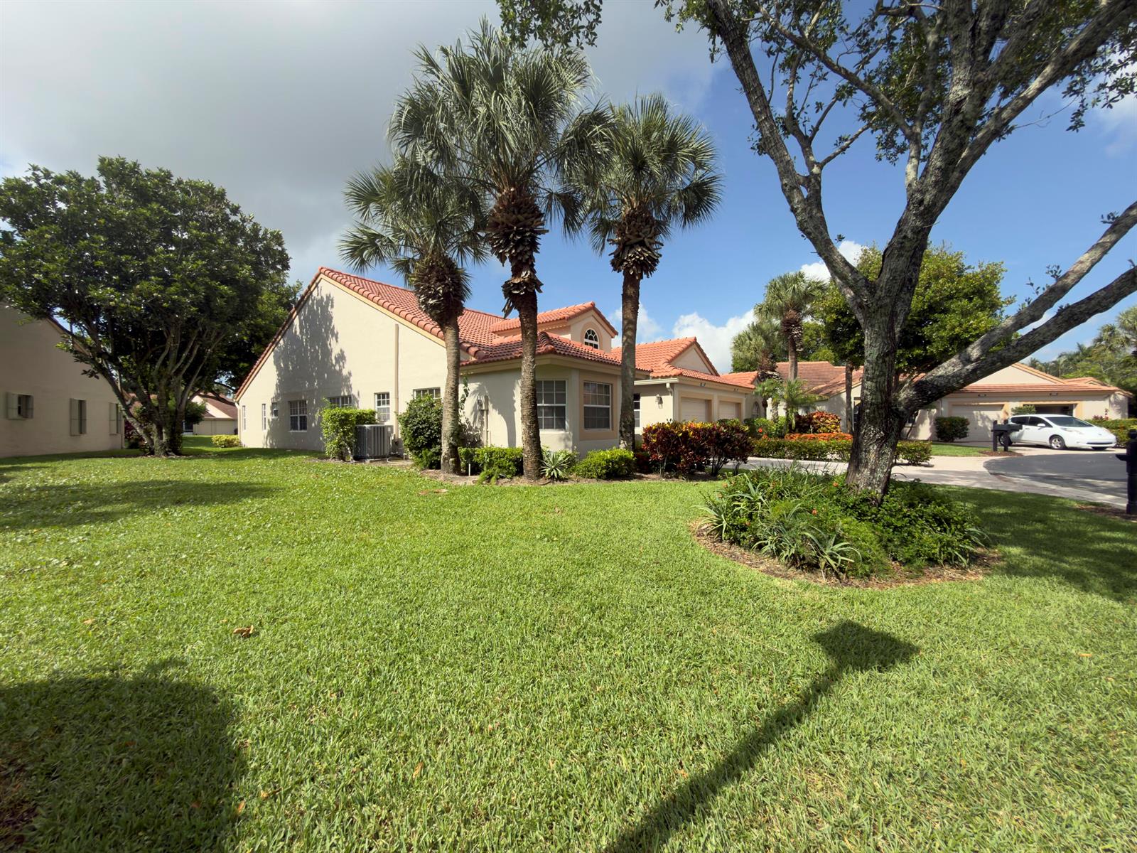 A beige house with a red tile roof and palm trees sits on a lawn — 7922 Sandy Pointe Drive, Delray Beach FL 33446, DELRAY BEACH, FL