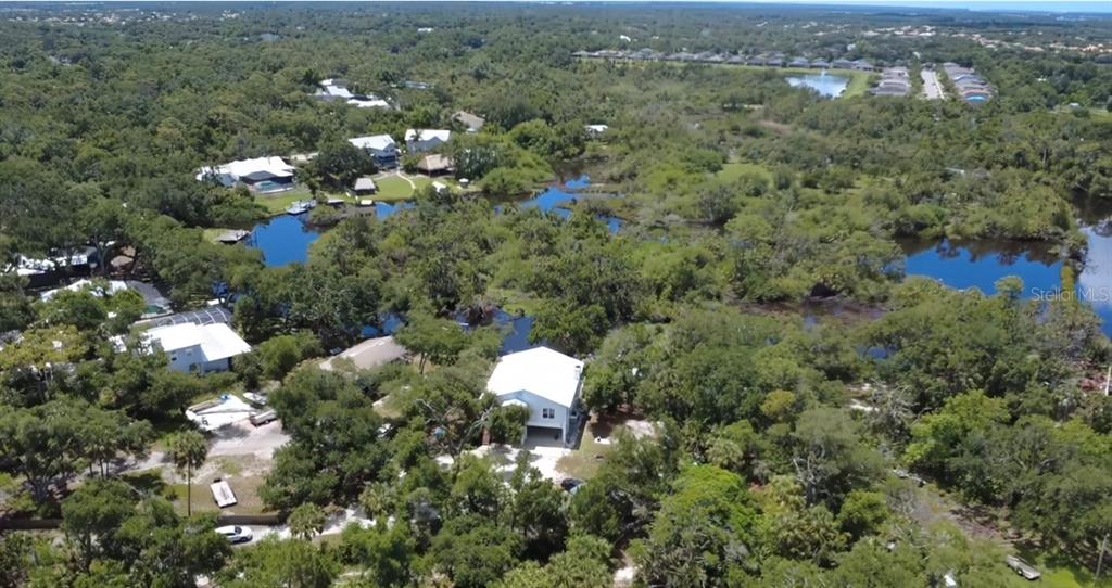 An aerial view shows a white house surrounded by dense trees and several small ponds — 1160 MILL CREEK, BRADENTON, FL