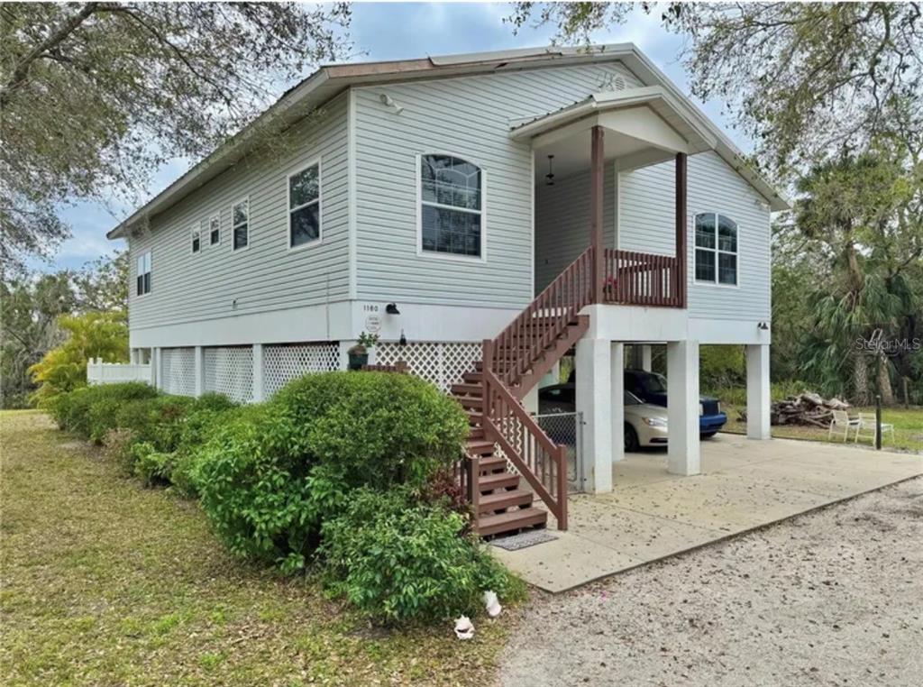 A light-colored elevated house with a front staircase, covered parking, and lattice skirting — 1160 MILL CREEK, BRADENTON, FL