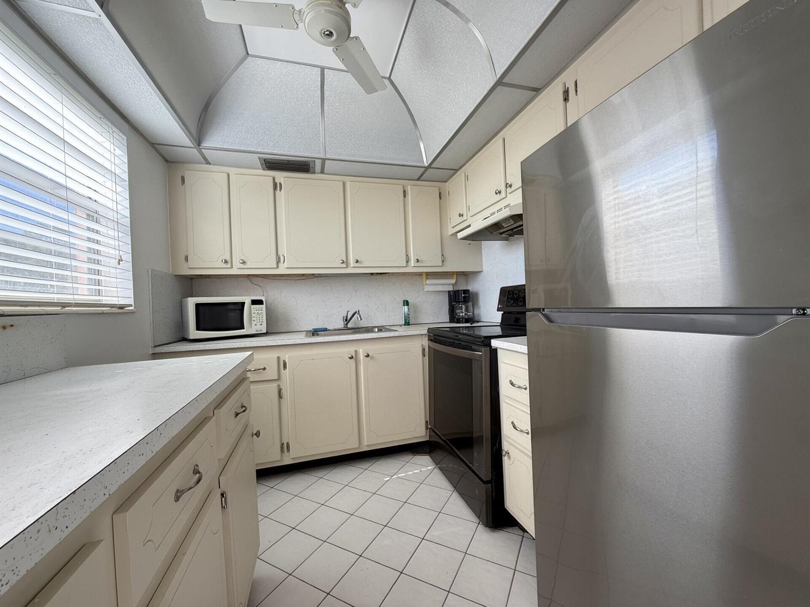 A kitchen features off-white cabinets, stainless steel appliances, a white tiled floor, and a ceiling fan — 9 Hastings A # 9, West Palm Beach FL 33417, WEST PALM BEACH, FL