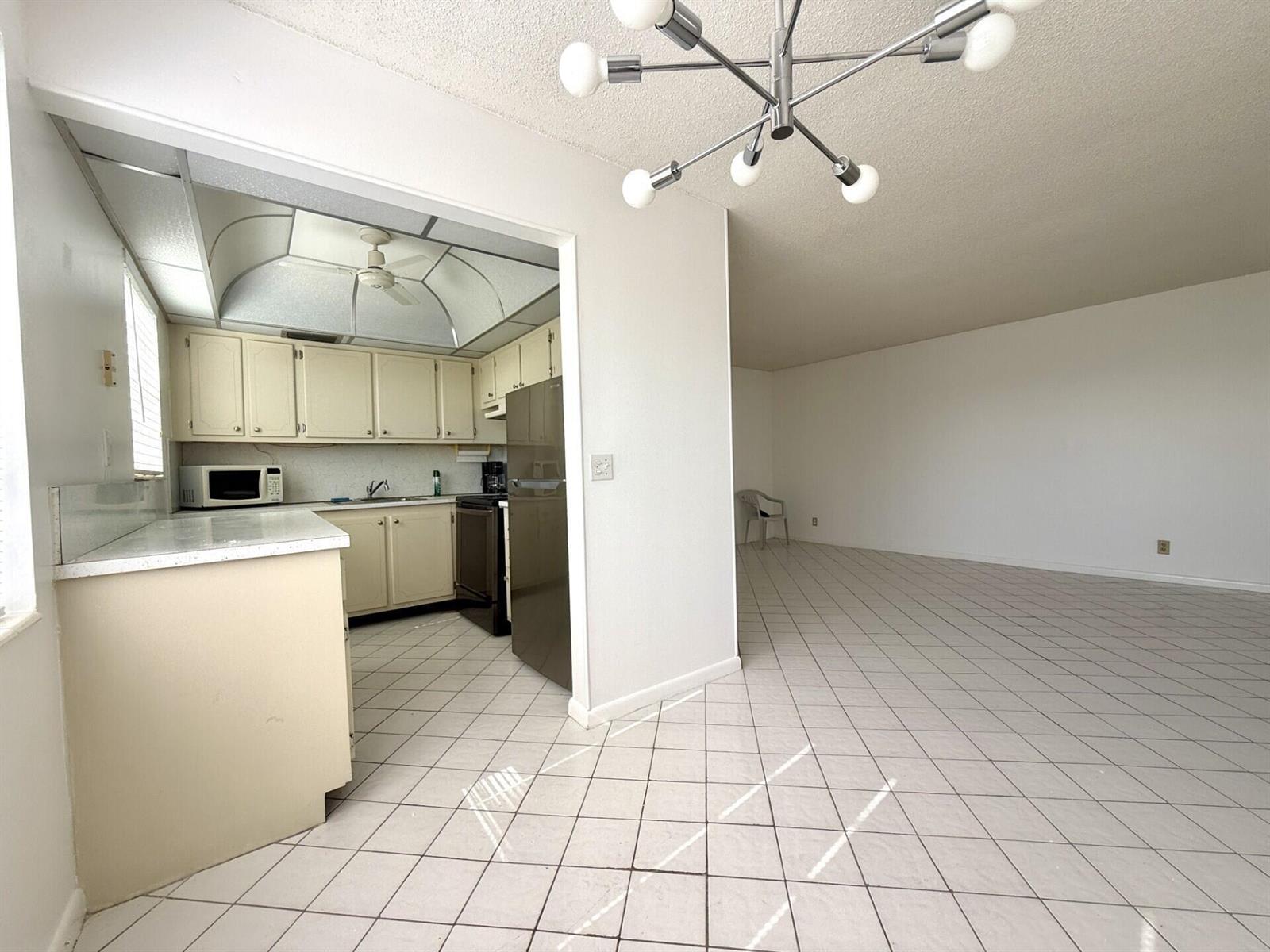 A kitchen with off-white cabinets and a tile floor opens into a large living area — 9 Hastings A # 9, West Palm Beach FL 33417, WEST PALM BEACH, FL