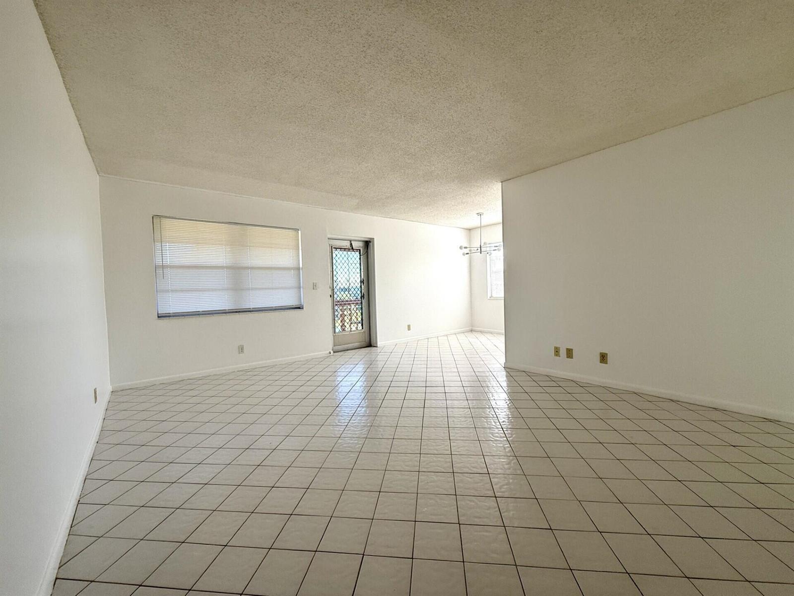 An empty room features white tiled floors, white walls, a popcorn ceiling, and a glass door — 9 Hastings A # 9, West Palm Beach FL 33417, WEST PALM BEACH, FL