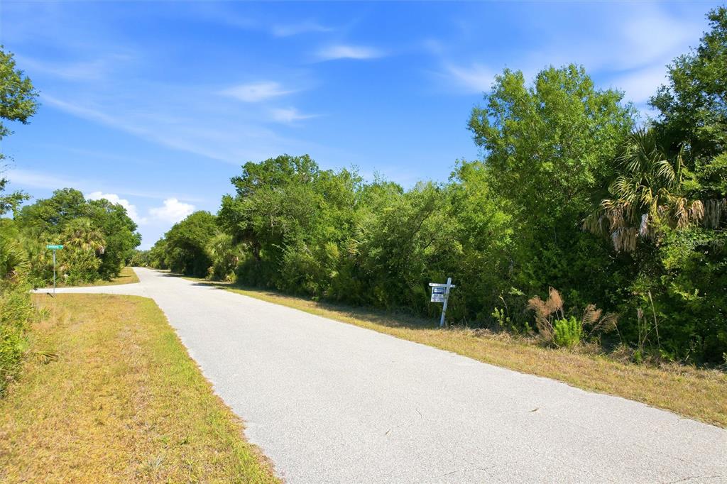 A paved road leads past a wooded lot with a real estate sign — 7095 FREEBERG CIRCLE, PORT CHARLOTTE, FL