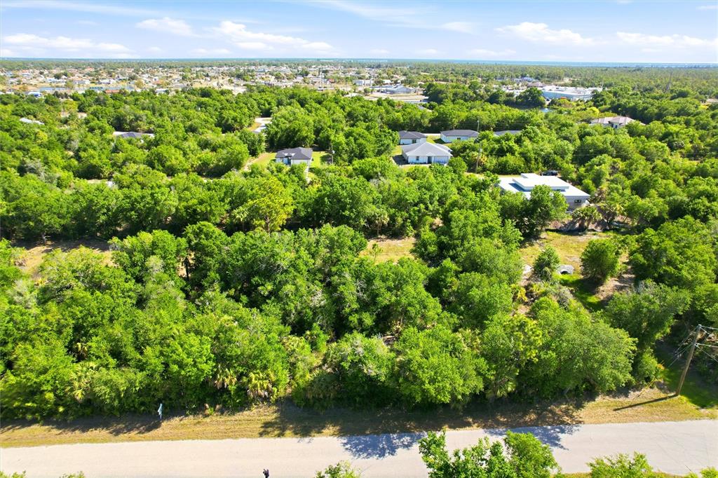 An aerial view shows a wooded lot bordered by a road with nearby houses — 7095 FREEBERG CIRCLE, PORT CHARLOTTE, FL