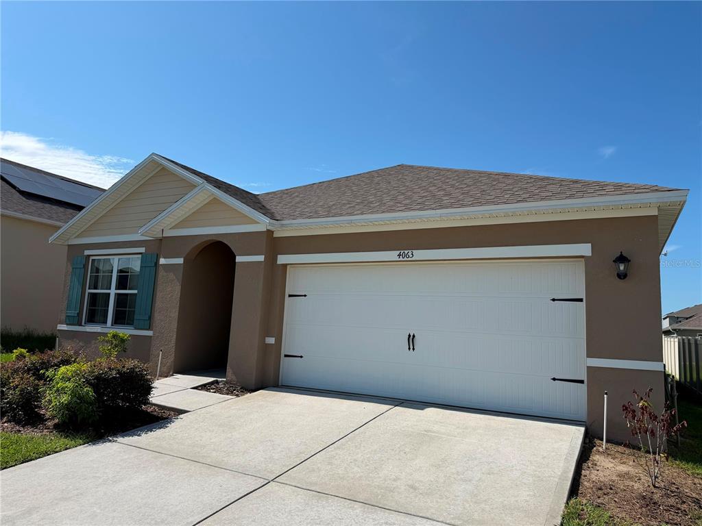 A single-story house with a tan stucco exterior, a white garage door, and teal shutters — 4063 ALISSA LANE, HAINES CITY, FL