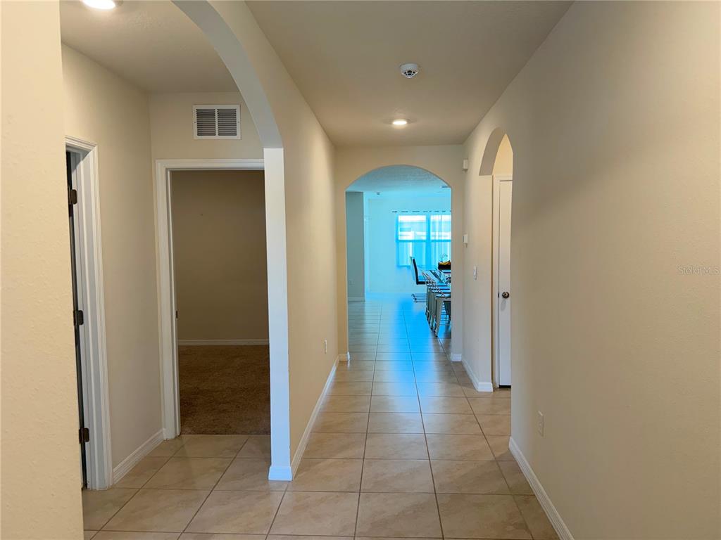 A tiled hallway leads past a carpeted room toward an open living area with windows — 4063 ALISSA LANE, HAINES CITY, FL