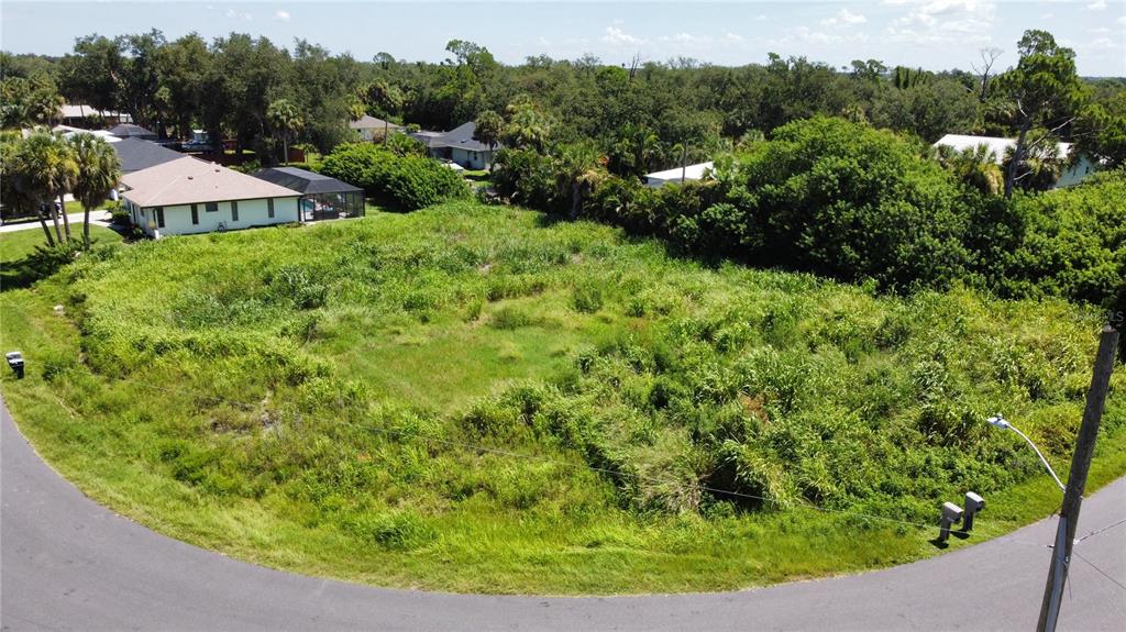 An aerial view shows a vacant, overgrown residential lot situated along a curved paved road — 18450 GOODMAN CIRCLE, PORT CHARLOTTE, FL