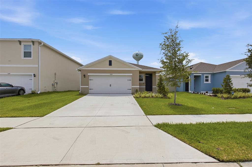 A single-story suburban house with a tan exterior, a two-car garage, and a concrete driveway — 3638 MARLBERRY WAY, SANFORD, FL