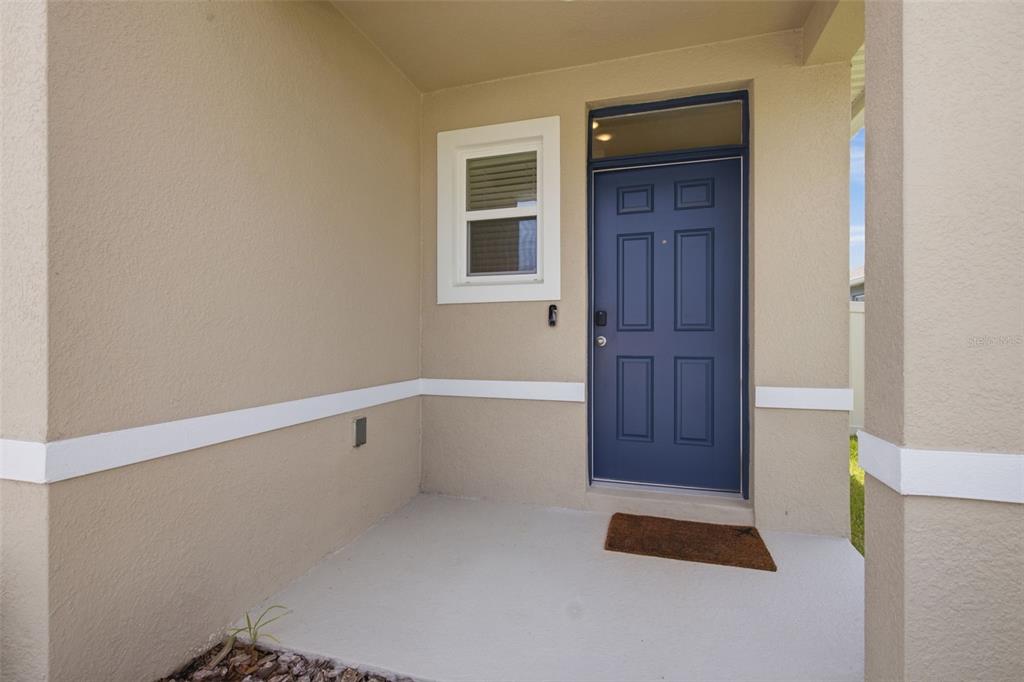 A blue front door with a transom window sits on a covered concrete porch — 3638 MARLBERRY WAY, SANFORD, FL