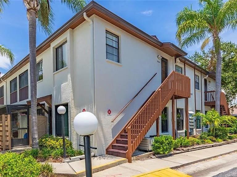 A two-story apartment building features white stucco walls, brown trim, and an exterior wooden staircase — 2829 74TH STREET W UNIT 2829, BRADENTON, FL
