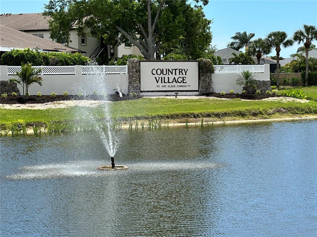 A fountain sits in a pond in front of a Country Village community sign — 2829 74TH STREET W UNIT 2829, BRADENTON, FL