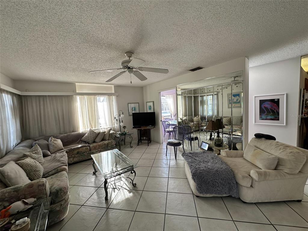 A living room features tiled floors, a ceiling fan, a mirrored wall, and neutral furniture — 2829 74TH STREET W UNIT 2829, BRADENTON, FL