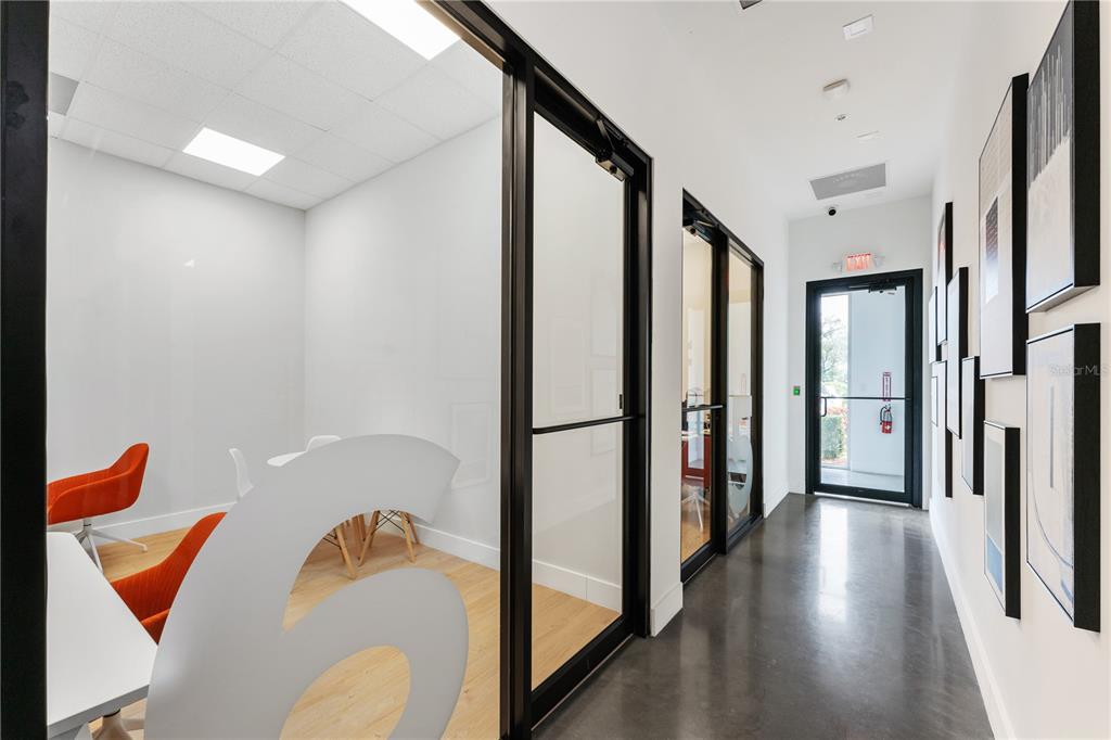 A modern office hallway with glass-walled conference rooms, polished concrete floors, and framed wall art — 7726 WINEGARD ROAD, ORLANDO, FL