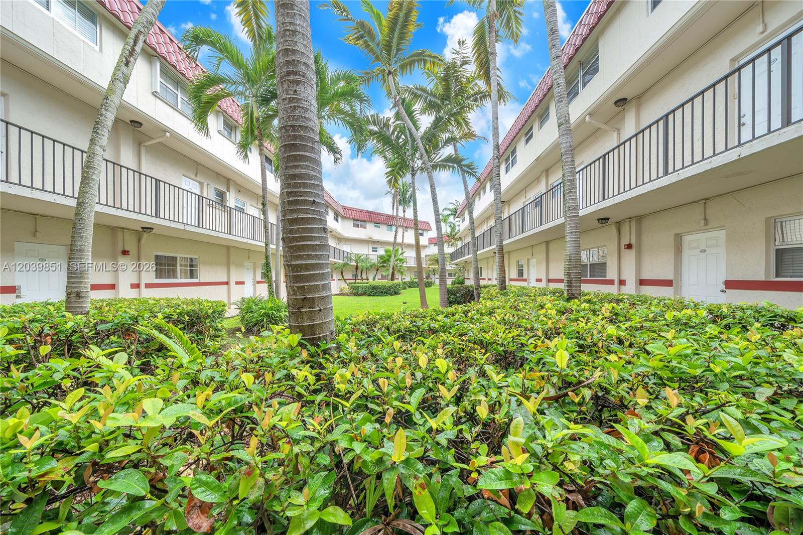 A courtyard with palm trees and lush landscaping sits between two multi-story apartment buildings — 8650 SW 67th Ave # 1010, Pinecrest FL 33156, PINECREST, FL