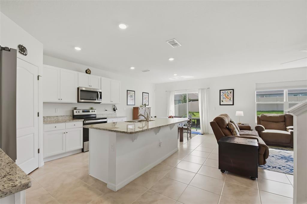 An open-concept kitchen with white cabinets, granite countertops, and an island overlooks a living area — 33428 COUNTRY HOUSE DRIVE, SORRENTO, FL