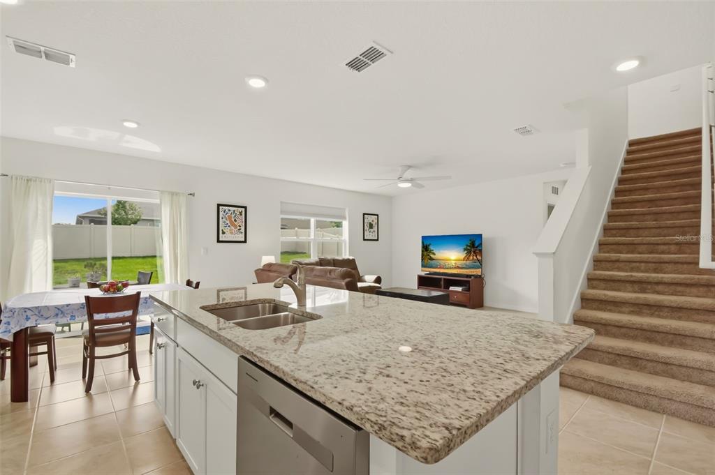 A kitchen island with granite countertops overlooks an open-concept living area with carpeted stairs — 33428 COUNTRY HOUSE DRIVE, SORRENTO, FL